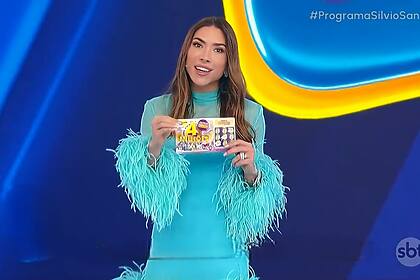 Patrícia Abravanel com vestido azul claro segurando a Tele Sena de Aniversário nas mãos