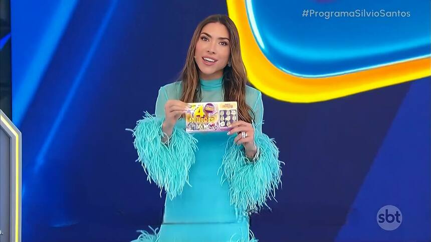 Patrícia Abravanel com vestido azul claro segurando a Tele Sena de Aniversário nas mãos