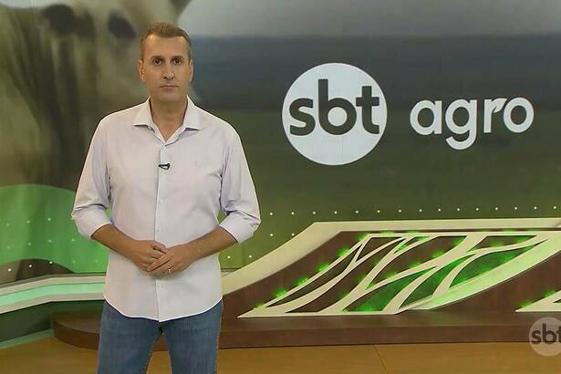 Sandro Ivanowski de camisa branca na frente do logo do SBT Agro no telão do SBT