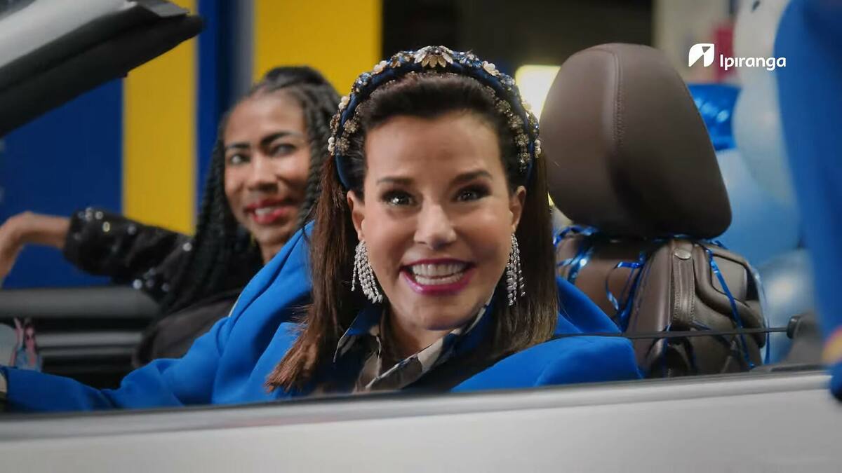 Inês Brasil ao lado de Narcisa, sorridentes, dentro de um carro, parado em um posto de gasolina do Ipiranga