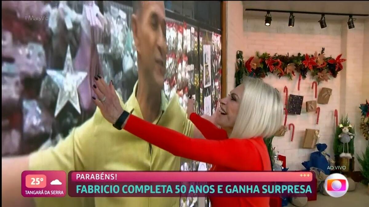 Ana Maria Braga abraçando o telão do Mais Você, simbolizando um abraço no repórter Fabricio Battaglini