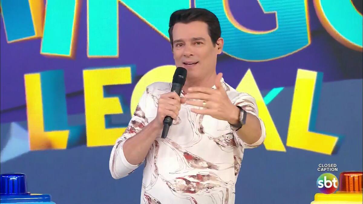 Celso Portiolli apresenta o Domingo Legal segurando microfone preto e com camisa clara estampada