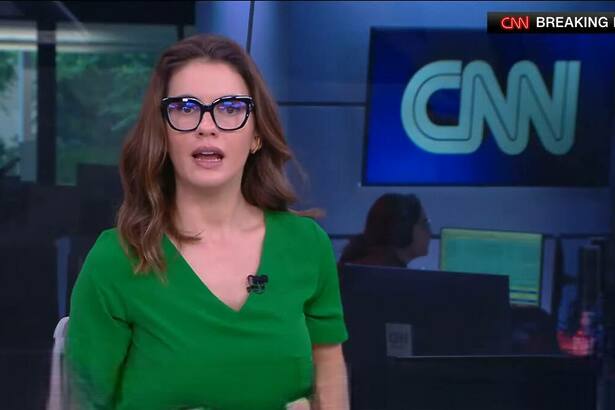 Elisa Veeck de óculos de grau e blusa verde na redação da CNN Brasil