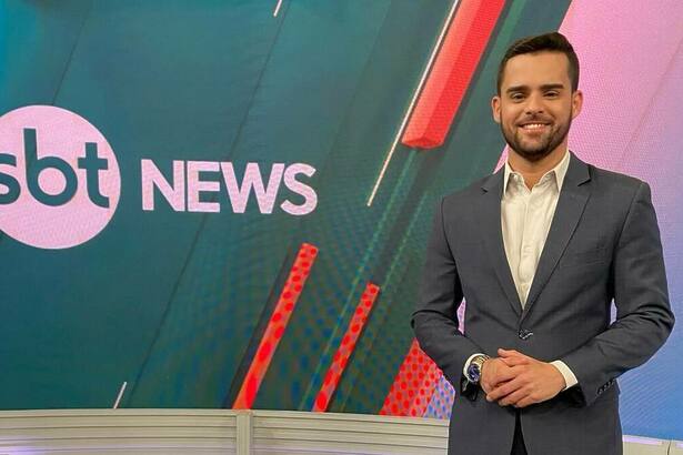 Lucas Carvalho -sorridente, em frente ao telão do SBT News