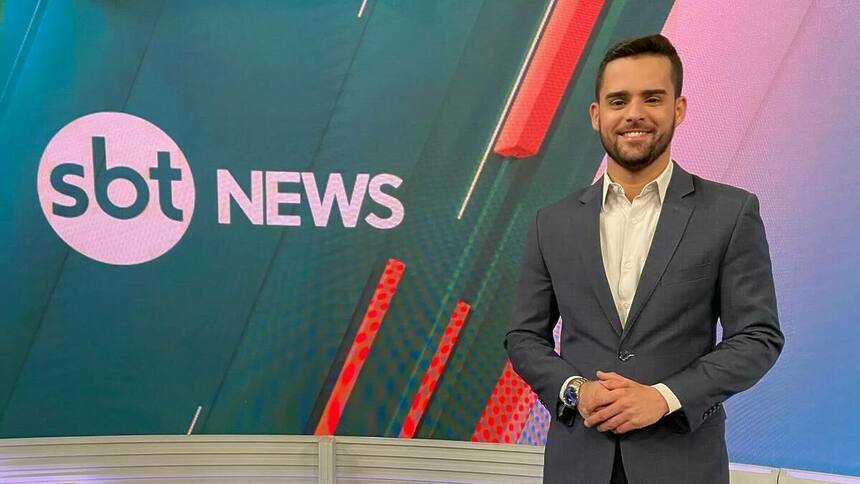 Lucas Carvalho -sorridente, em frente ao telão do SBT News