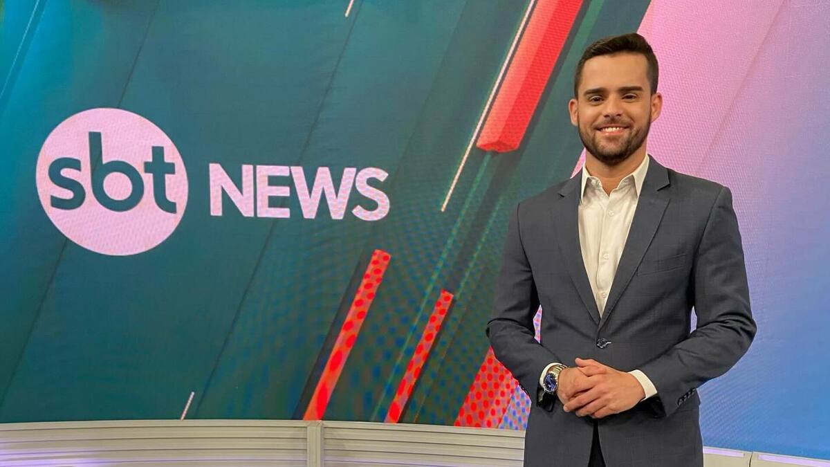 Lucas Carvalho -sorridente, em frente ao telão do SBT News