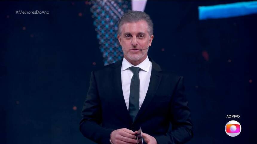 Luciano Huck, de terno e gravata, em trecho do Melhores do Ano