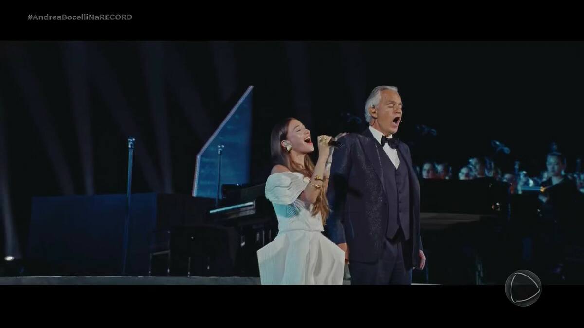 Mulher vestida de branco canta ao lado do Tenor Andrea Bocelli