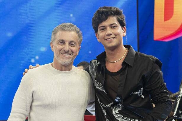 Luciano Huck ao lado de Leo Foguete sorrindo no palco do Domingão