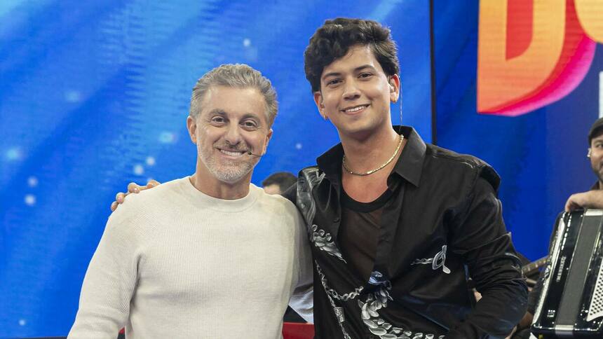 Luciano Huck ao lado de Leo Foguete sorrindo no palco do Domingão