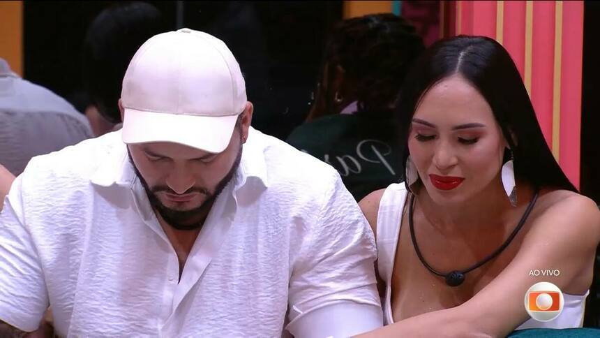 Marcelo com a cabeça baixa de boné branco e Arleane olhando para o chão no BBB 25