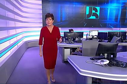 Christina Lemos de vestido vermelho caminha pela redação do Jornal da Record na abertura do telejornal