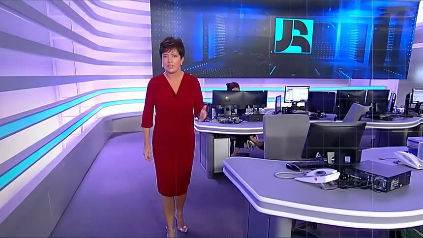 Christina Lemos de vestido vermelho caminha pela redação do Jornal da Record na abertura do telejornal