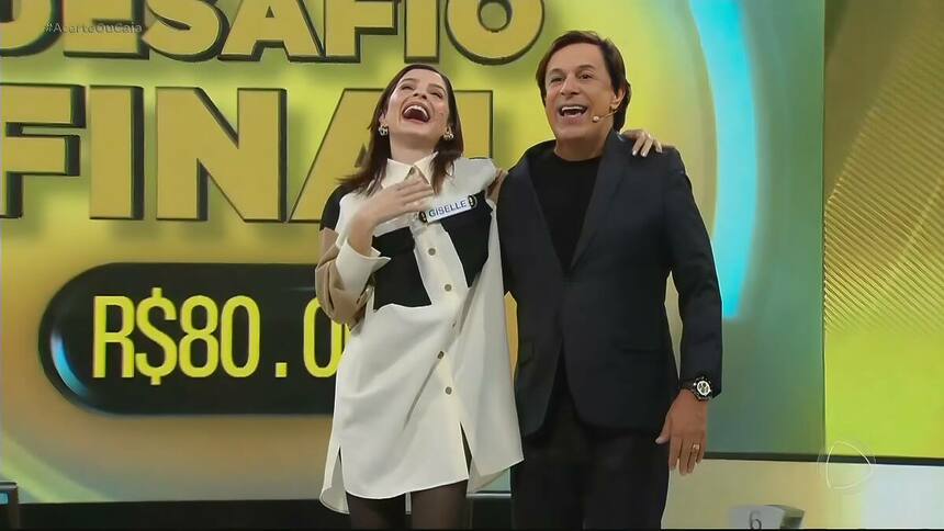 Giselle Batista sorrindo e comemorando vitória no Acerte ou Caia! ao lado de Tom Cavalcante