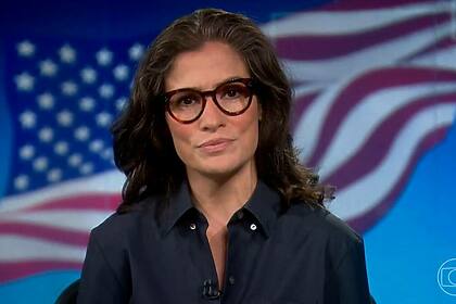 Renata Vasconcellos, em trecho do Jornal Nacional, com a bandeira dos Estados Unidos ao fundo