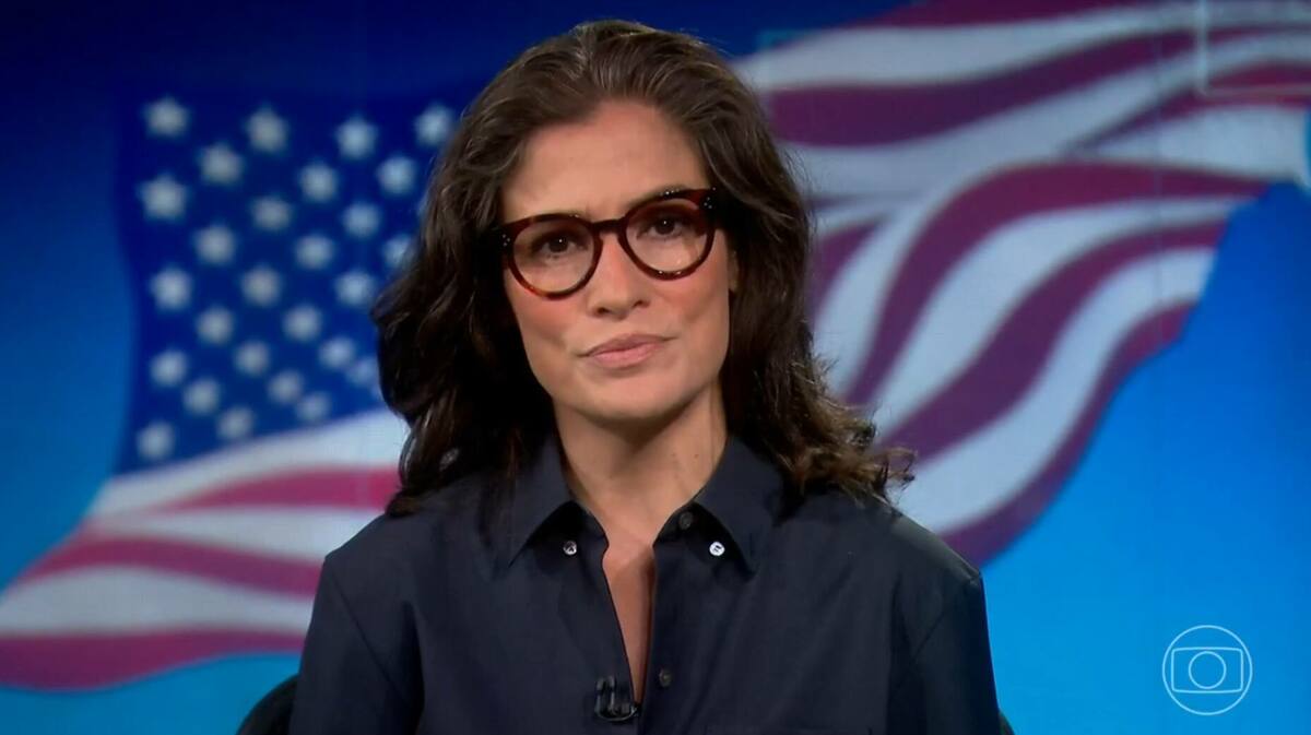 Renata Vasconcellos, em trecho do Jornal Nacional, com a bandeira dos Estados Unidos ao fundo