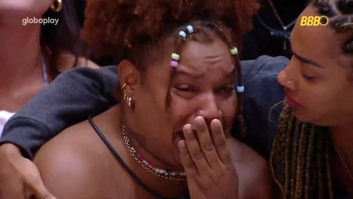 Camilla chora com lágrimas no rosto e a mão na boca, sendo consolada por Aline na sala do BBB 25