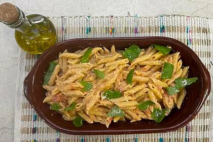 Penne à la vodka na tigela marrom ao lado de um pote de azeite no cenário do É de Casa