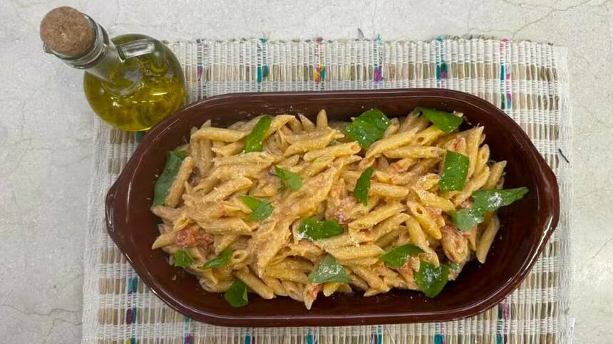 Penne à la vodka na tigela marrom ao lado de um pote de azeite no cenário do É de Casa