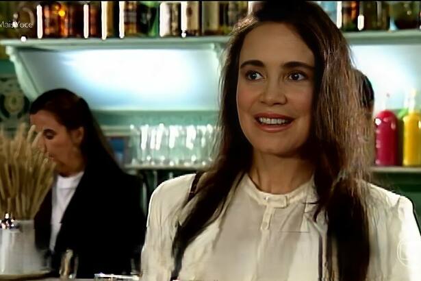 Regina Duarte com blusa branca em cena, sorridente, em cena da novela História de Amor
