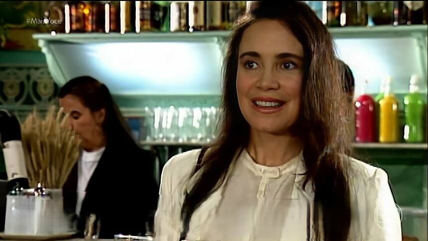 Regina Duarte com blusa branca em cena, sorridente, em cena da novela História de Amor