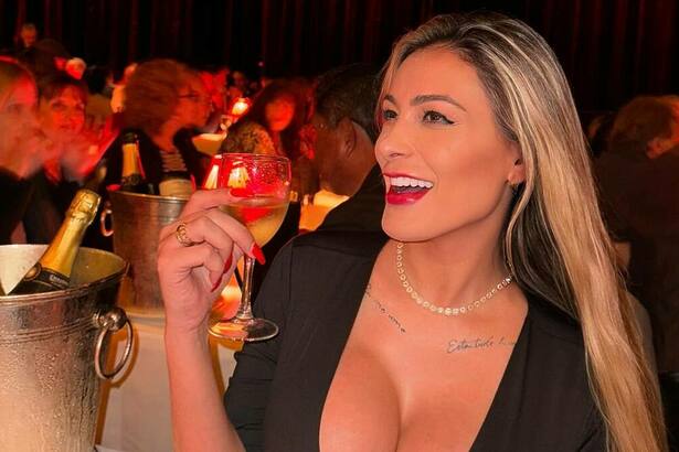 Andressa Urach sorridente, com a taça de vinho na mão