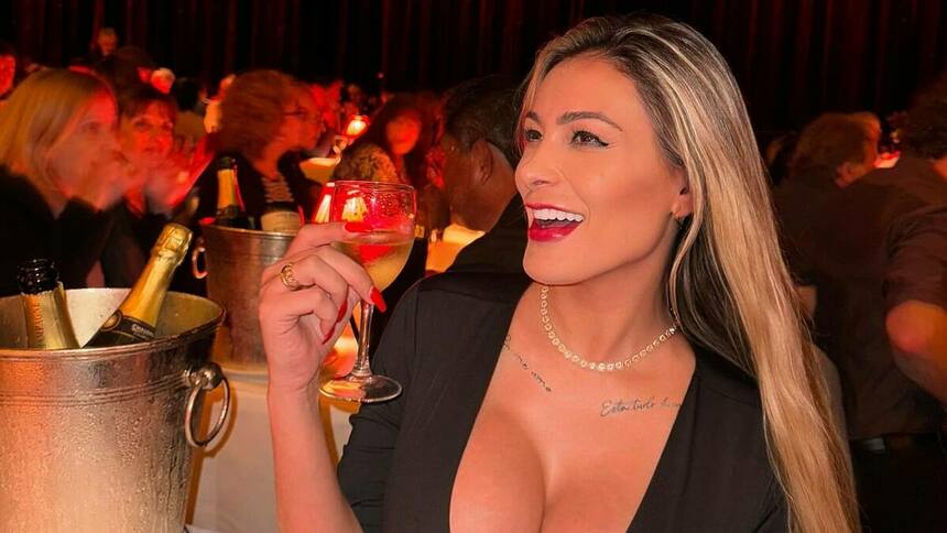 Andressa Urach sorridente, com a taça de vinho na mão