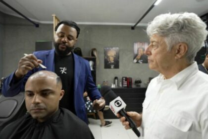 Caco Barcellos ao lado de um cliente e um barbeiro, em uma barbearia, em trecho do Profissão Repórter