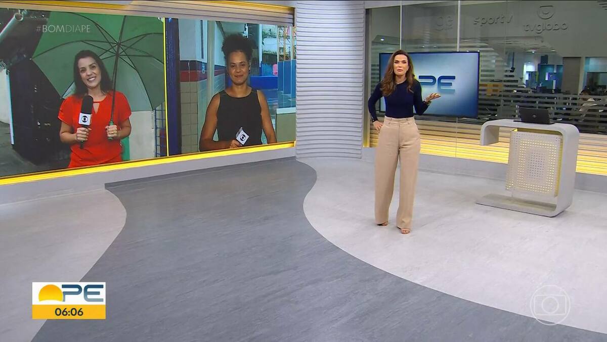 Clarissa Góes de blusa azul e calça nude andando pelo cenário do Bom Dia PE