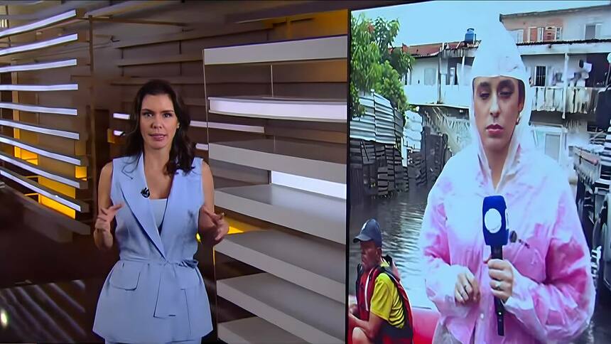 Camila Busnello veste conjunto azul e se aproxima do telão do Fala Brasil para conversar ao vivo com repórter da RECORD que está com capa de chuva e em um bote salva-vidas