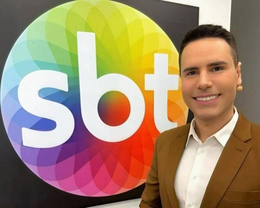 Logo do SBT no quadro do camarim onde Luiz Bacci aparece de terno marrom e microfonado