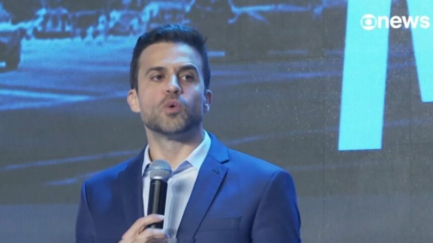 Pablo Marçal segura microfone. Ele veste terno e camisa clara azul em reportagem da GloboNews
