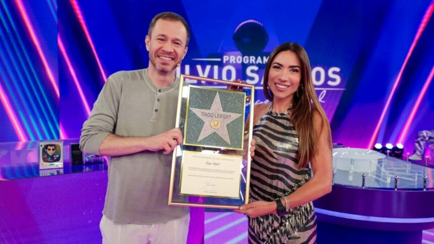 Tiago Leifert ao lado de Patricia Abravanel, mostrando o contrato assinado no Programa Silvio Santos