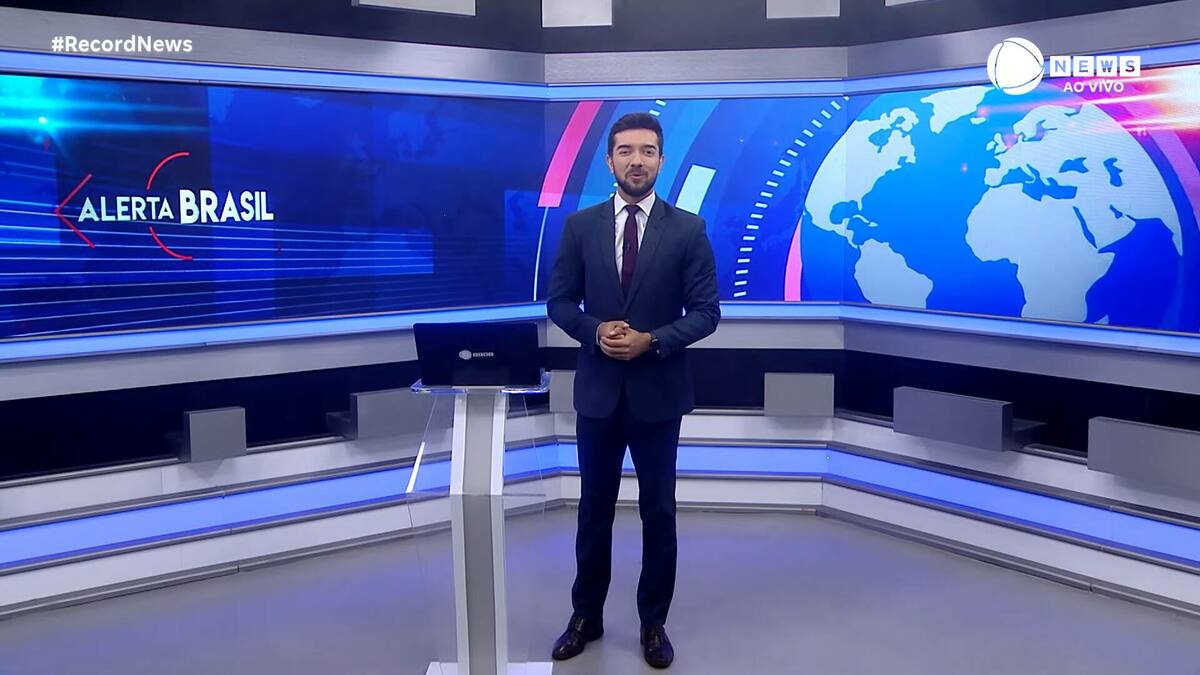 Jhonatan Mazini em pé, vestindo terno e gravata, no centro do novo cenário da Record News