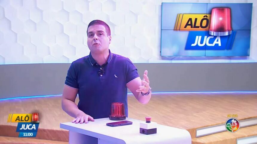 Marcelo Castro em frente a bancada do seu programa Alô Juca que tem uma sirene no cenário do programa da TV Aratu/SBT