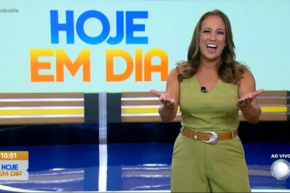 Renata Alves sorrir em frente ao logo do programa Hoje em Dia. Apresentadora veste um conjunto verde