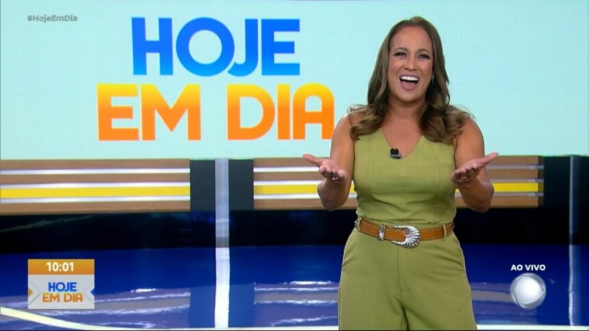 Renata Alves sorrir em frente ao logo do programa Hoje em Dia. Apresentadora veste um conjunto verde