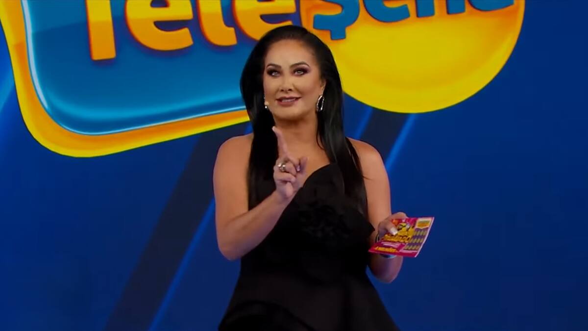 Helen Ganzaolli segura bilhete da Tele Sena de Carnaval 2025. Ela está de vestido preto no cenário do SBT