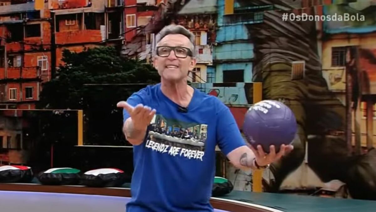 Craque Neto surtado e com uma bola na mão no cenário de Os Donos da Bola