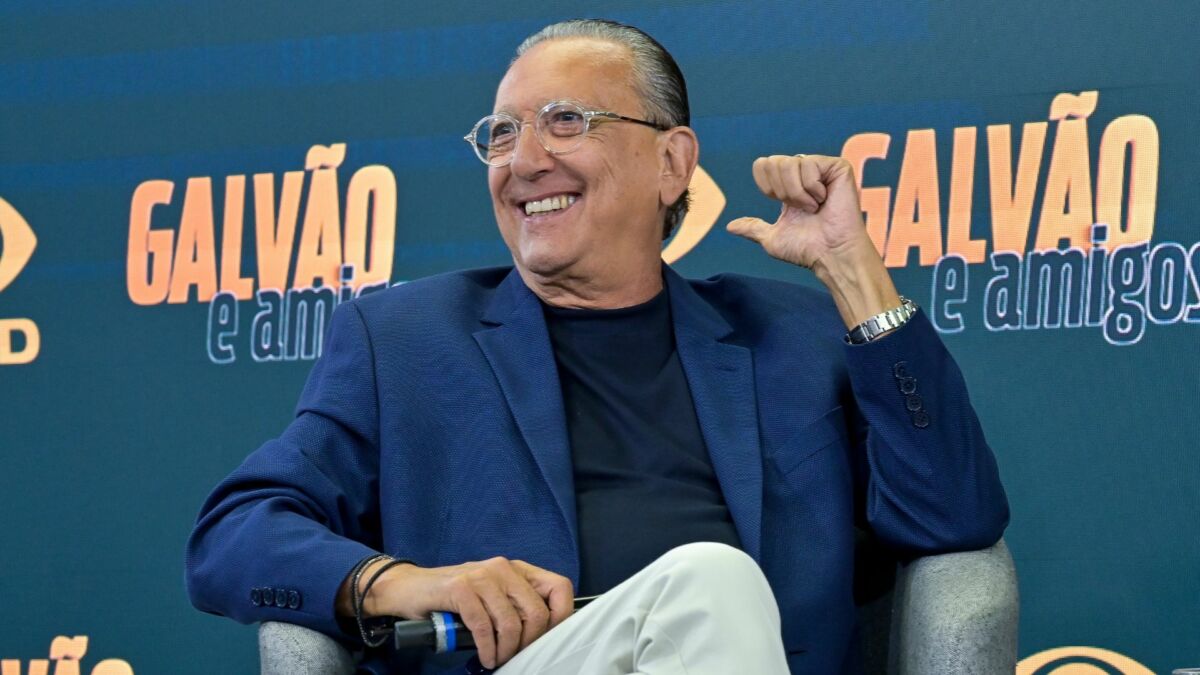 Galvão Bueno sorridente, sentado em uma poltrona, em trecho da coletiva