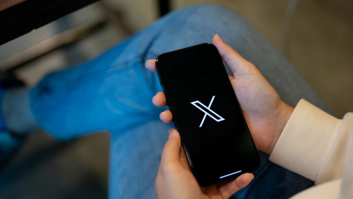 Pessoa com um celular em mãos mostrando o logo da rede social X