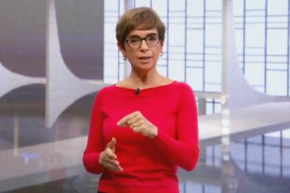 Renata Lo Prete, vestindo suéter vermelho, no cenário do Jornal da Globo