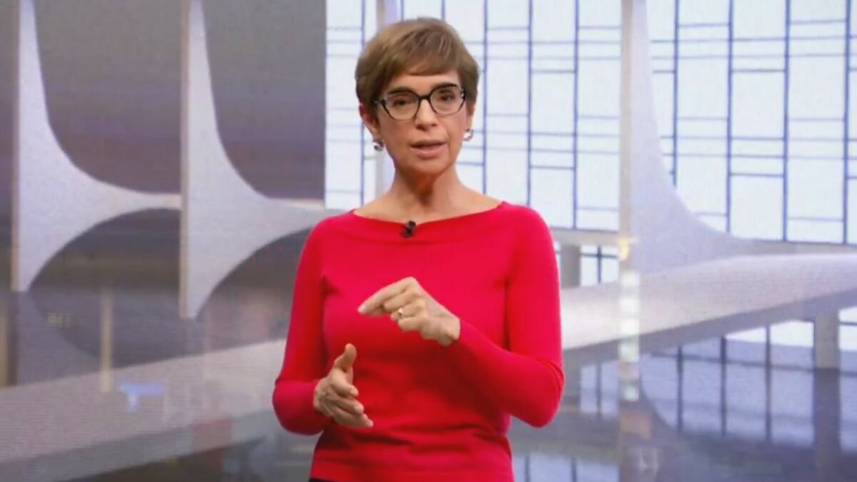 Renata Lo Prete, vestindo suéter vermelho, no cenário do Jornal da Globo