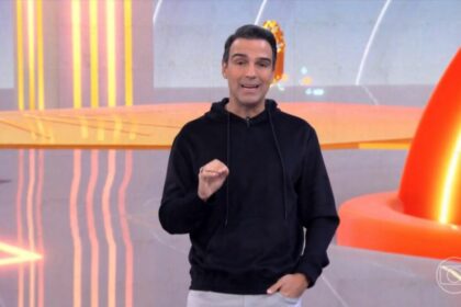 Tadeu Schmidt de macacão preto no cenário do BBB 25