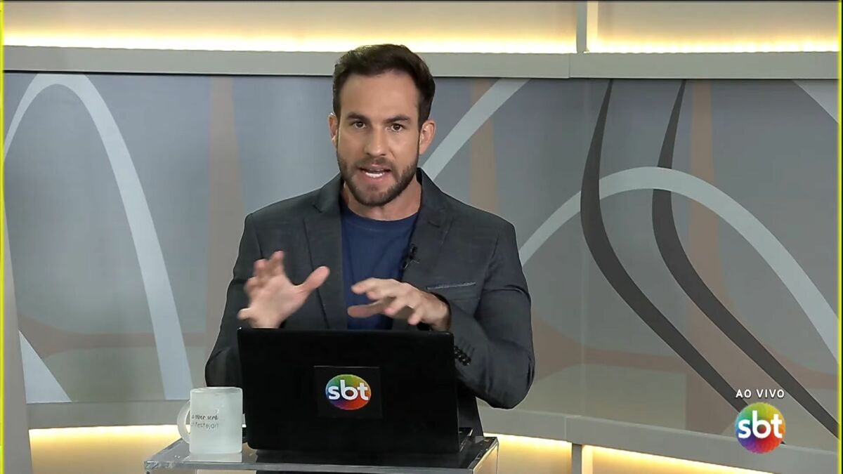 Daniel Adjuto com as mãos levantadas sobre o notebook no cenário do SBT Brasília