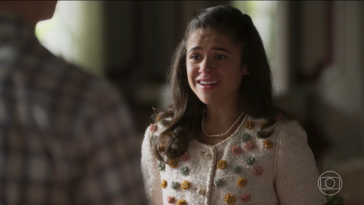 Bia com roupa branca florida, olha para Beto e sorrir em cena da novela Garota do Momento