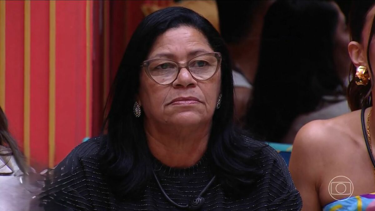 Delma olha sério para o telão onde Tadeu aparece na sala do BBB 25