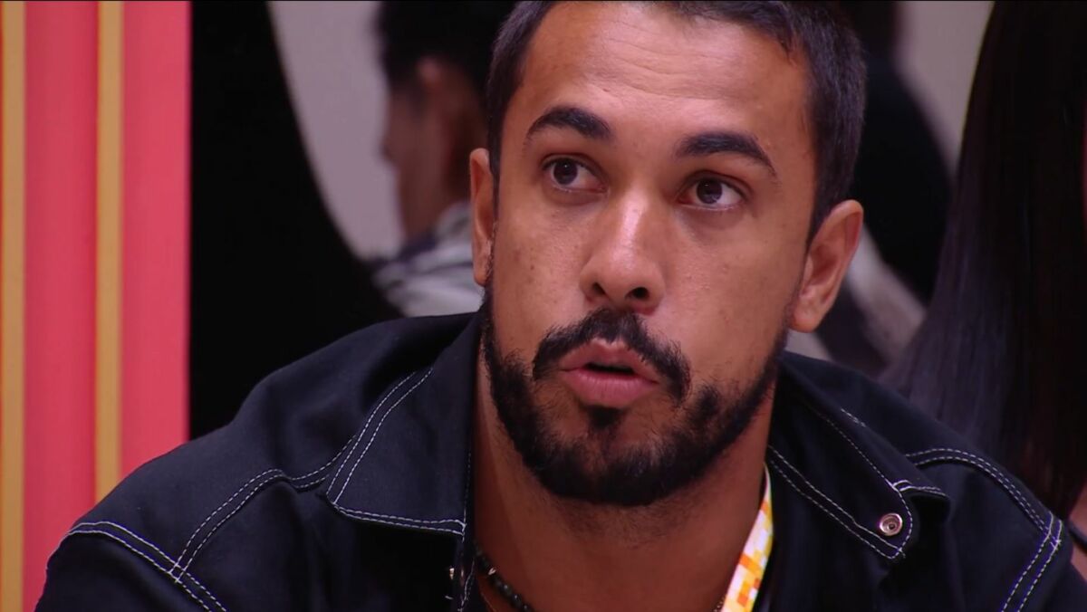 Maike com o colar do líder no pescoço sentadono sofá da sala do BBB 25 falando de Vinicius, barrado da festa do líder
