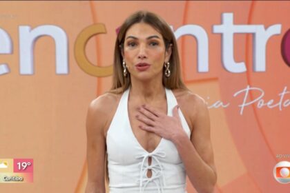 Patrícia Poeta de vestido branco e com a mão no peito no palco do Encontro