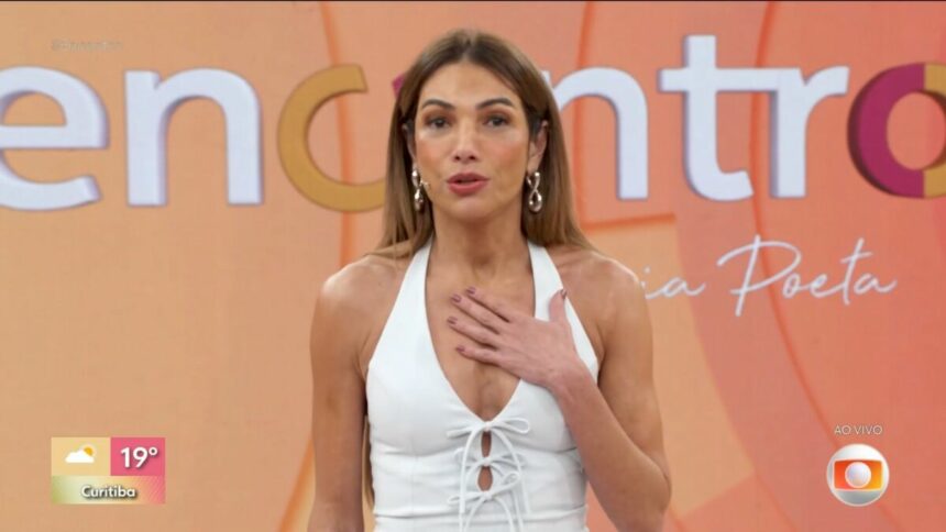 Patrícia Poeta de vestido branco e com a mão no peito no palco do Encontro